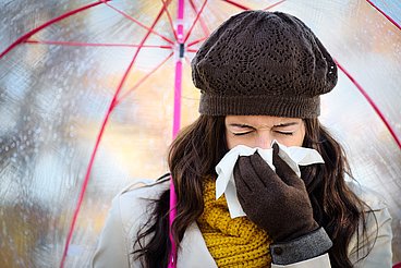 Hier sieht man eine erkältete Frau, im Regen, die niest. © Dirima / Fotolia.com